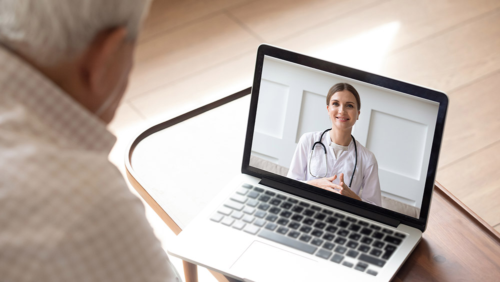 A doctor having a virtual visit with an elderly patient via a laptop.