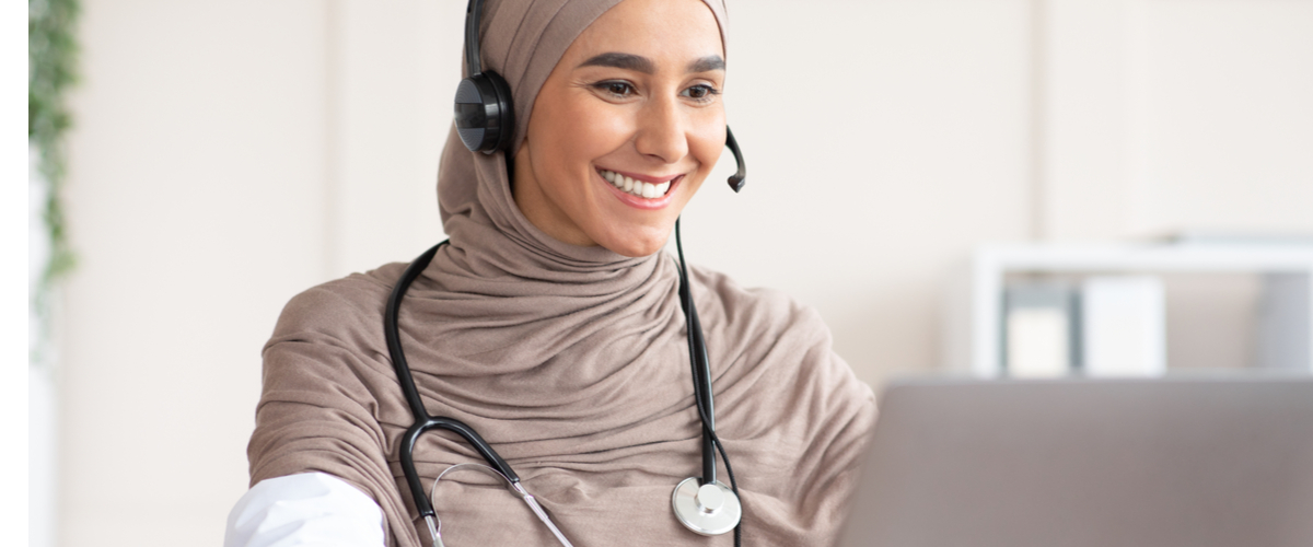 Female doctor wearing a headset looking and smiling at her laptop
