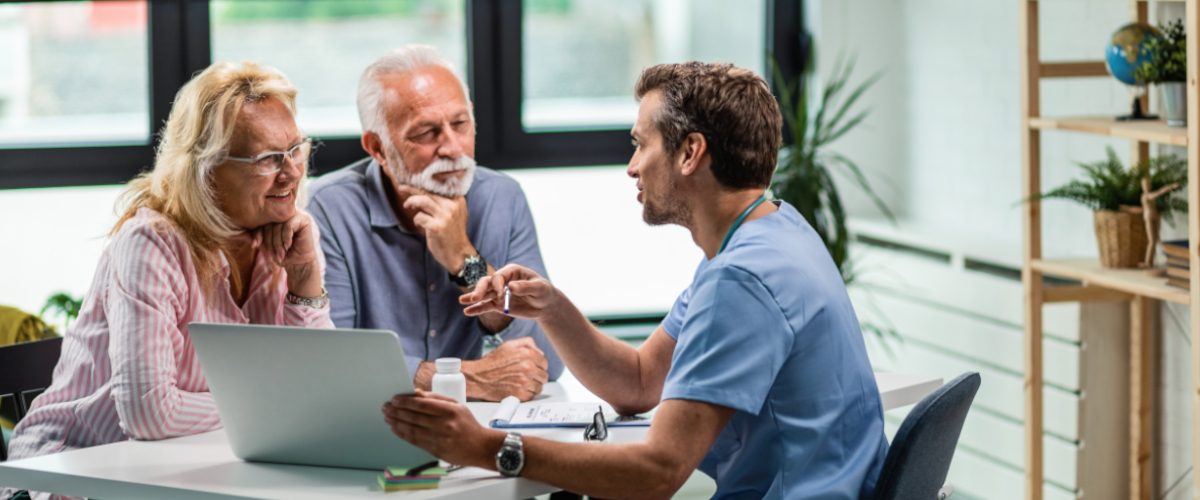 A doctor speaks with an elderly couple at his desk.