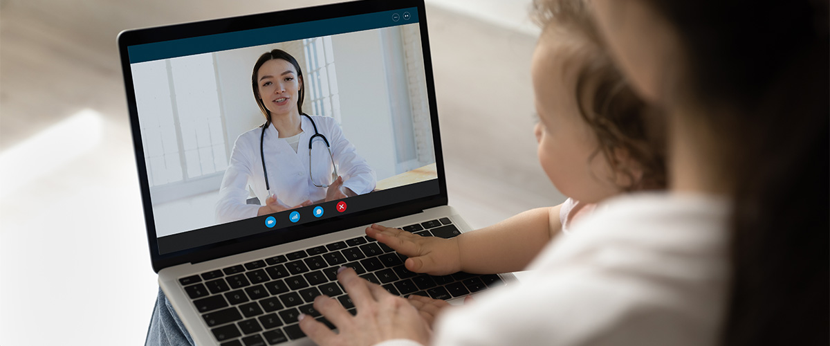 Mother sitting with child and laptop conducting a virtual health appointment
